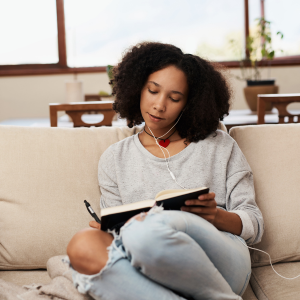 Black woman writing in journal sitting on a sofa.