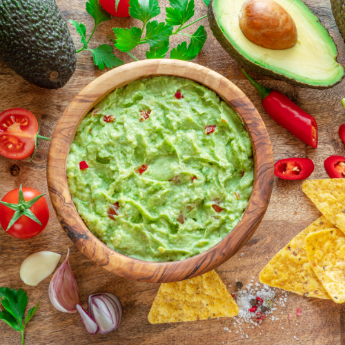 Guacamole in a wooden bowl surrounded by chips.