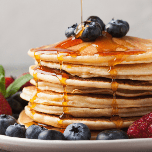 Stack of pancakes with drizzled maple syrup and blueberries.