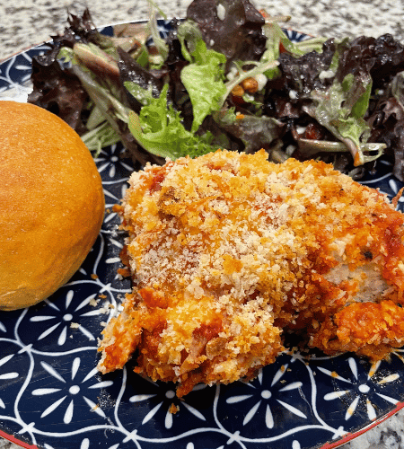 Plated chicken parmesan meatballs with a side salad and sweet potato rolls.