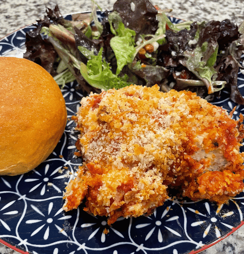 Plated chicken parmesan meatballs with a side salad and sweet potato rolls.